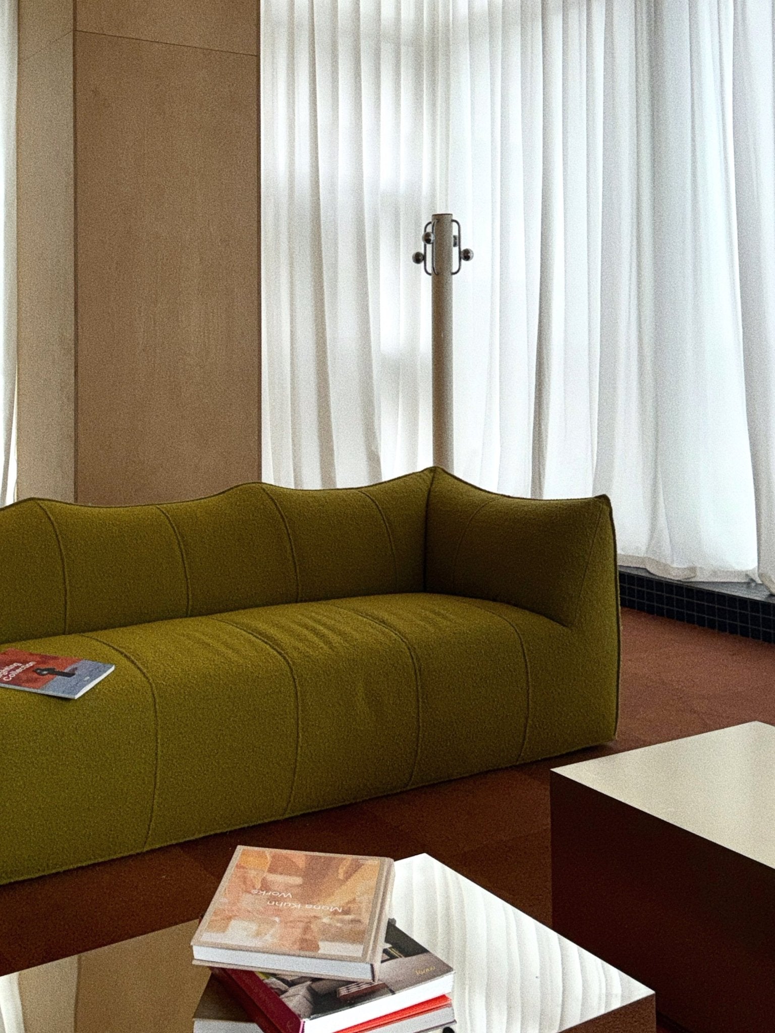 Modern living room with olive green sofa, glass coffee table, books, and sheer curtains